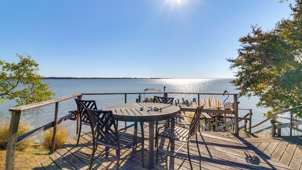 Eine Holzterrasse mit rundem Tisch und Stühlen mit Blick auf ein Gewässer.
