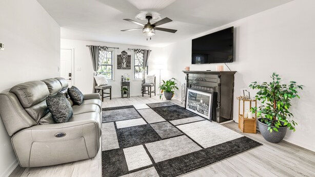 A modern living room with a sofa, a fireplace, a ceiling fan, and a flat-screen TV.