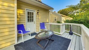 A deck with a glass-top table and two blue chairs, a white door, and a small porch area.