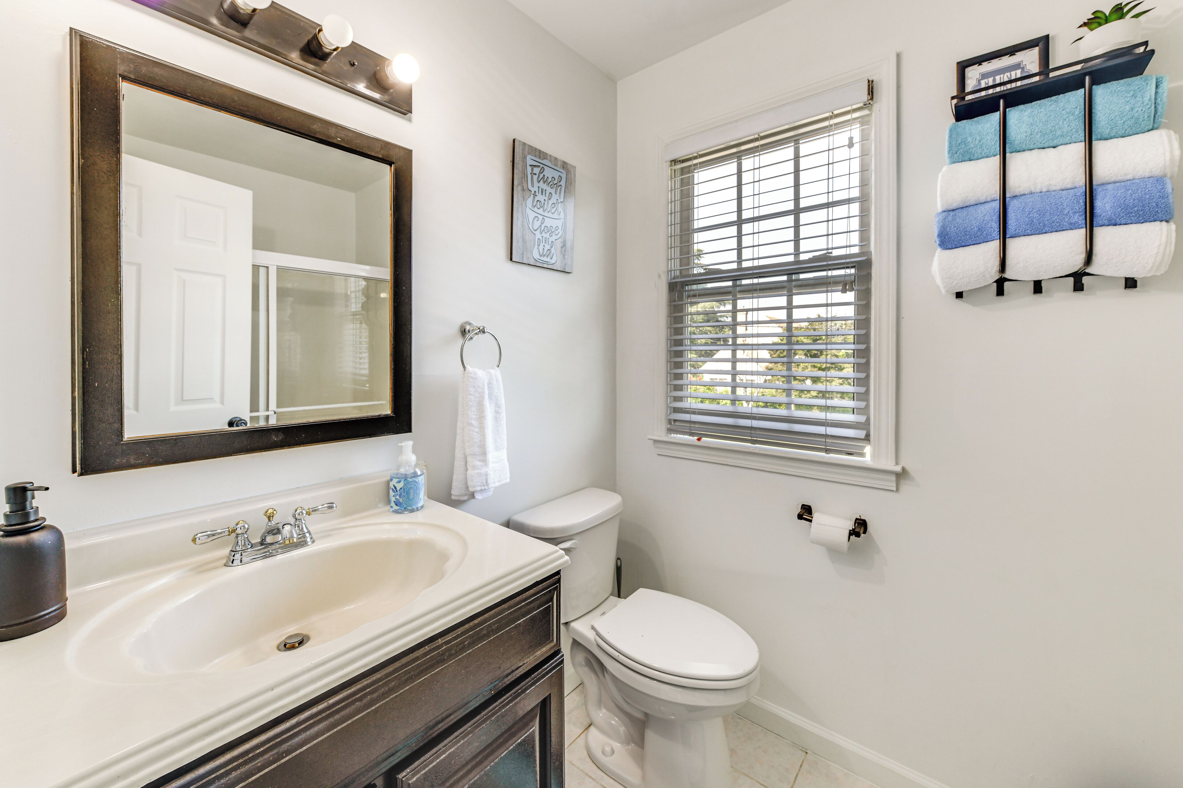 A bathroom with a sink, mirror, toilet, and window.