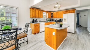 A modern kitchen with wooden cabinets, a central island, and a dining area with metal chairs.
