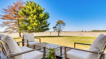 An outdoor seating area with wicker chairs and a table, surrounded by a grassy lawn and trees.