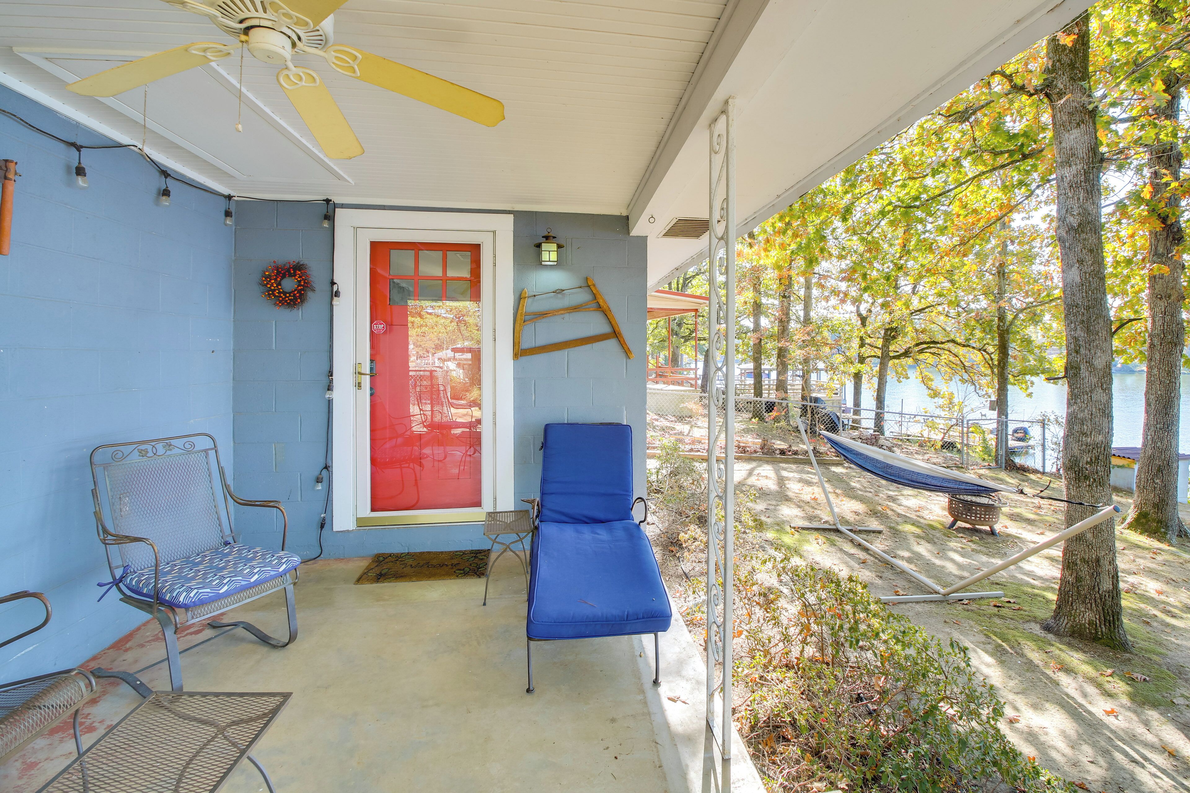 A covered porch with two blue lounge chairs, a red door, and a hammock.