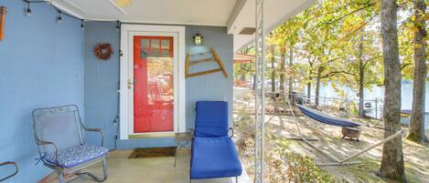 A covered porch with two blue lounge chairs, a red door, and a hammock.