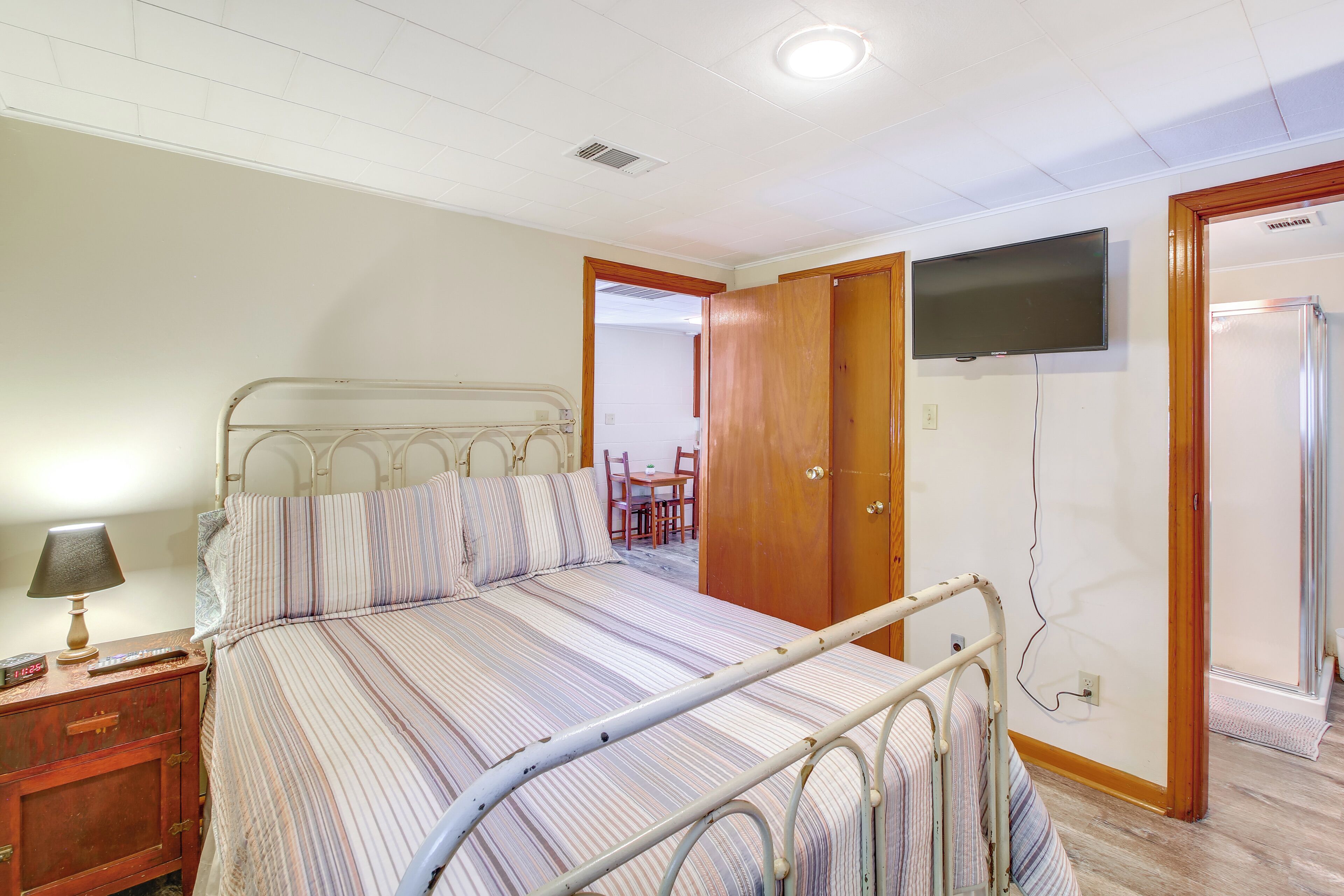 A bedroom with a bed, bedside table, lamp, and a television mounted on the wall.