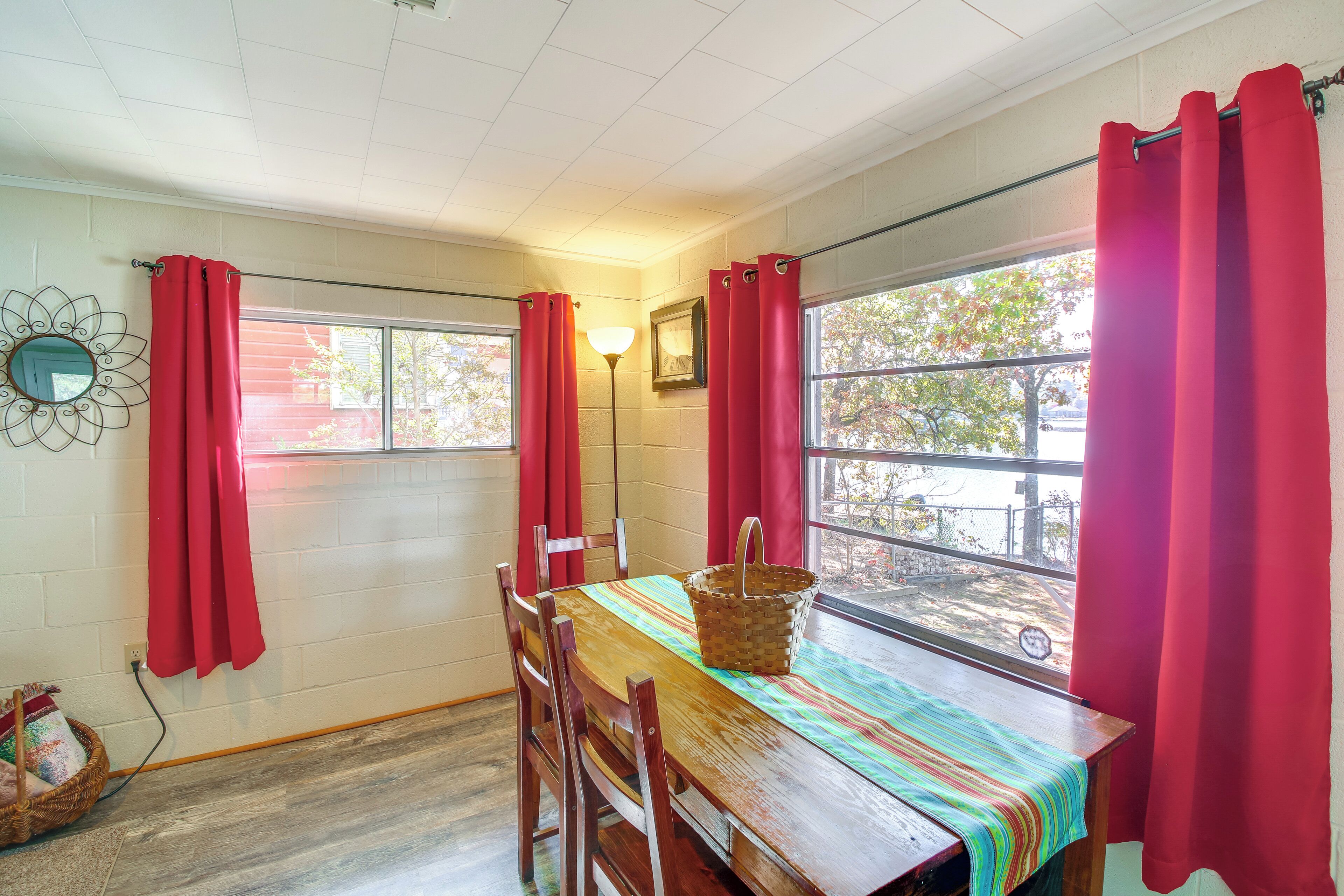 A dining area with a wooden table, red curtains, and a window with a view of trees.