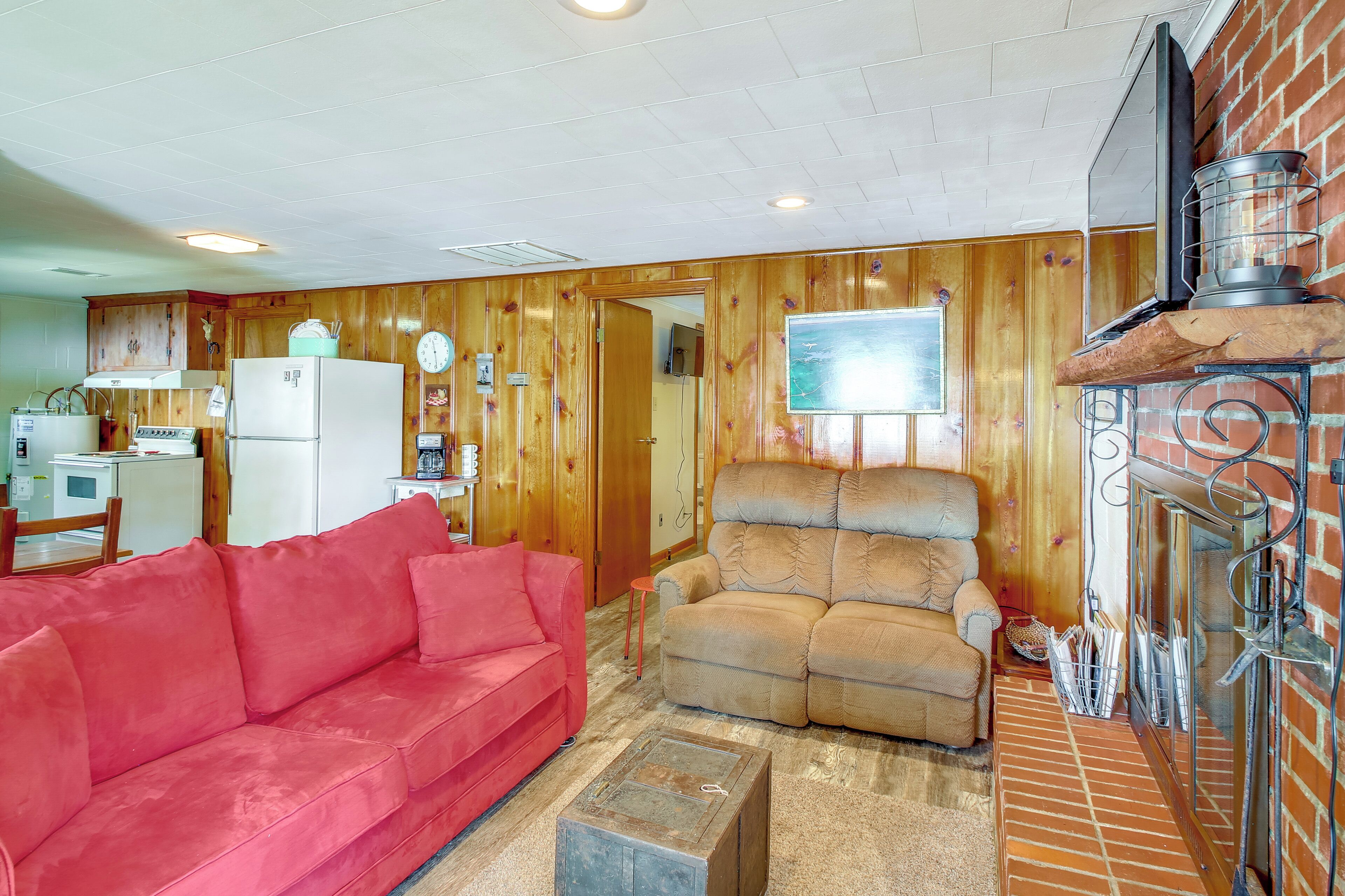 Uma sala de estar acolhedora com um sofá vermelho, uma poltrona bege e uma lareira.
