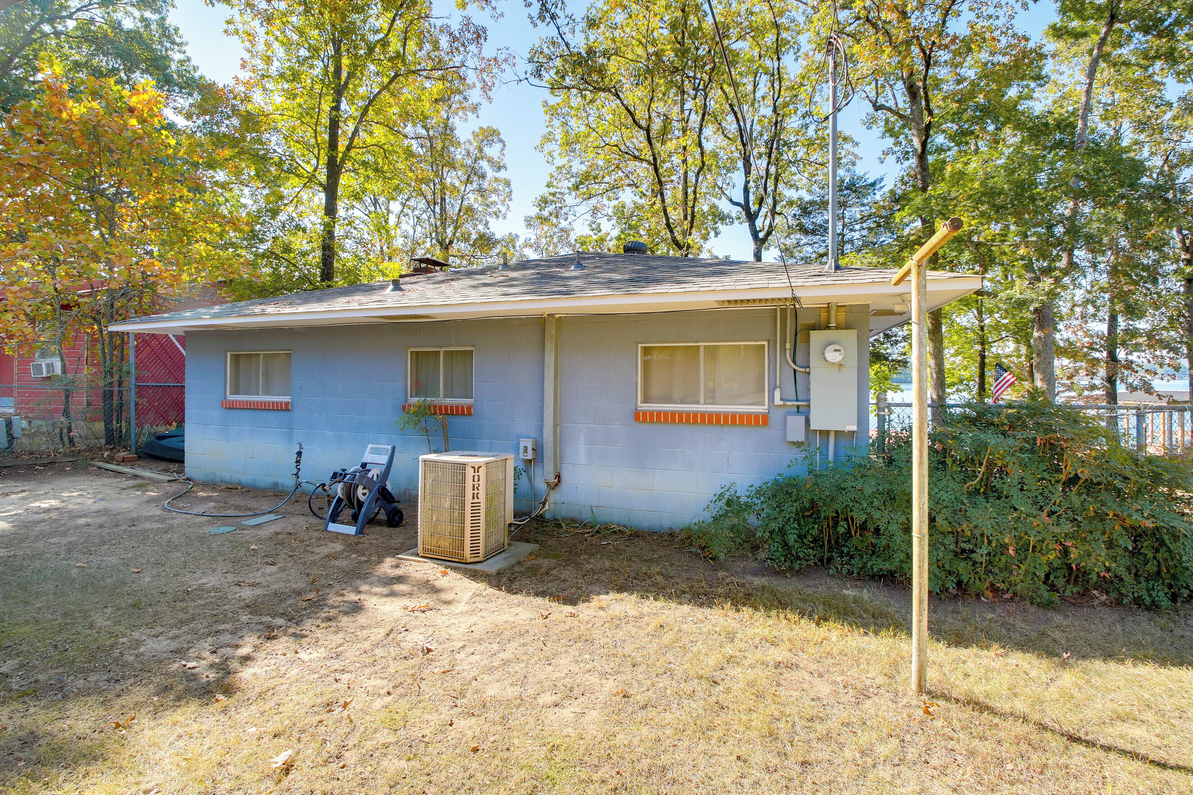 A single-story house with a garage, a small attached shed, and a yard with dry grass and trees.
