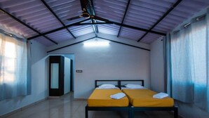 Une chambre avec deux lits, un ventilateur de plafond et une porte donnant sur une autre chambre.