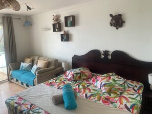 A bedroom with a bed, a sofa, a window with curtains, and wall decorations including a bird and a turtle. - "Ti Kaz An Nou" Studio with Ocean View - Marie Galante - Not Overlooked (Sainte-Anne)