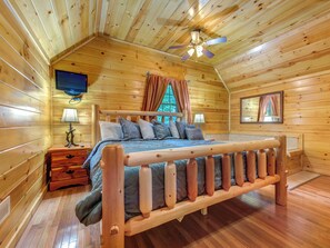 A wooden cabin bedroom with a bed, a nightstand, a television, and a ceiling fan. - 1BR, hot tub, jacuzzi.  Free attraction tickets! (Gatlinburg)