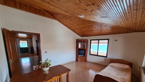 A bedroom with a wooden ceiling, a bed, a TV stand, and a window. - Tirane Tranquility Cottage (Paskuqan)