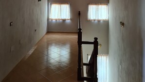 A spacious room with a sloped wooden ceiling and two windows with curtains. - Tirane Tranquility Cottage (Paskuqan)