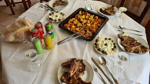A dining table set with plates of food, including roasted potatoes, steak, and a dessert with olives. There are also cans of soda and a bag of bread. - Tirane Tranquility Cottage (Paskuqan)