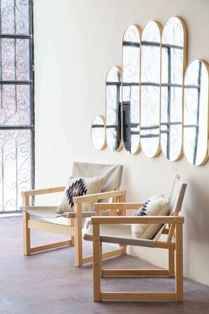 Ein Zimmer mit zwei Holzstühlen, einem großen Spiegel mit markantem Design und einem Fenster mit schmiedeeisernen Verzierungen.
