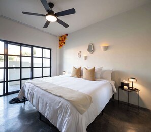 Ein modernes Schlafzimmer mit einem großen Bett, einem Deckenventilator, einem Fenster und einem Nachttisch mit Lampe.