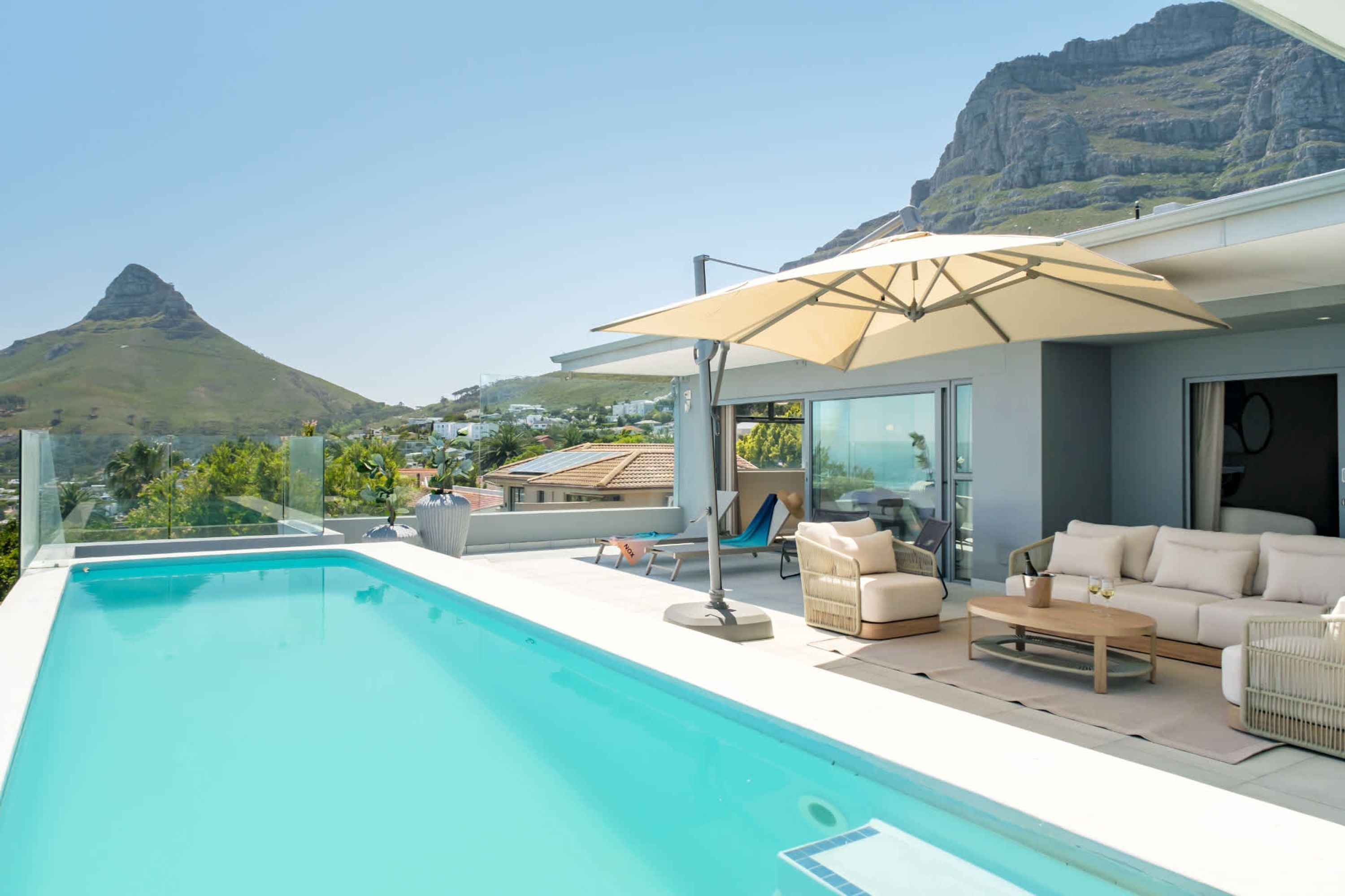 A modern outdoor pool area with a clear view of a mountain in the background, a lounge chair, and a sofa.