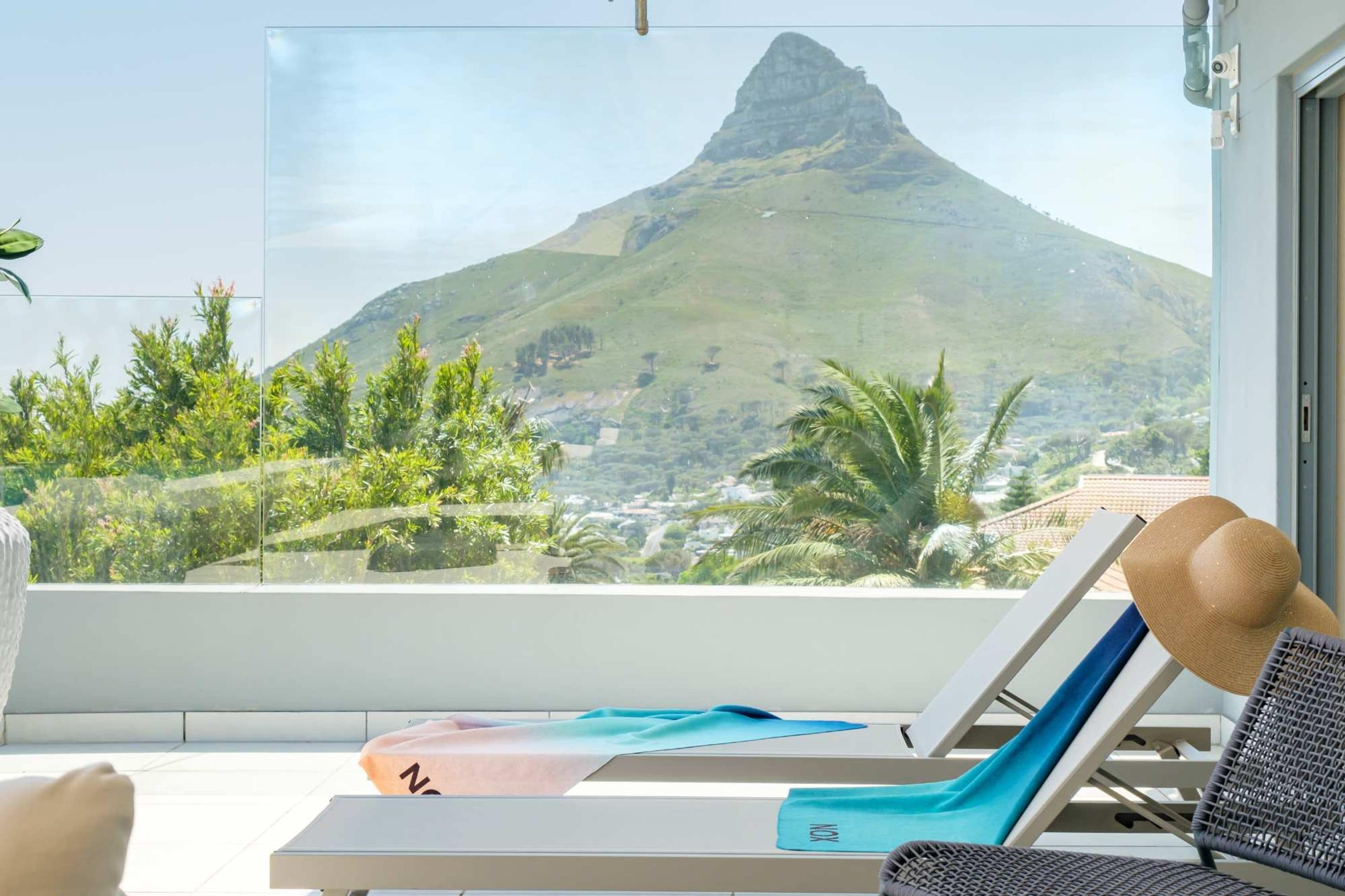A balcony with a view of a mountain, lounge chairs, and a yoga mat.