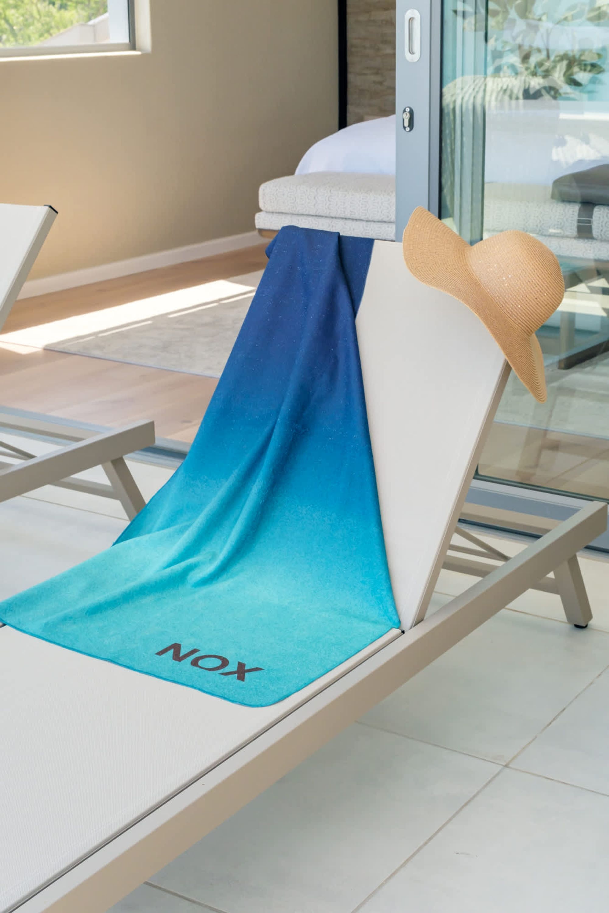 A sun lounger with a blue towel and a straw hat.