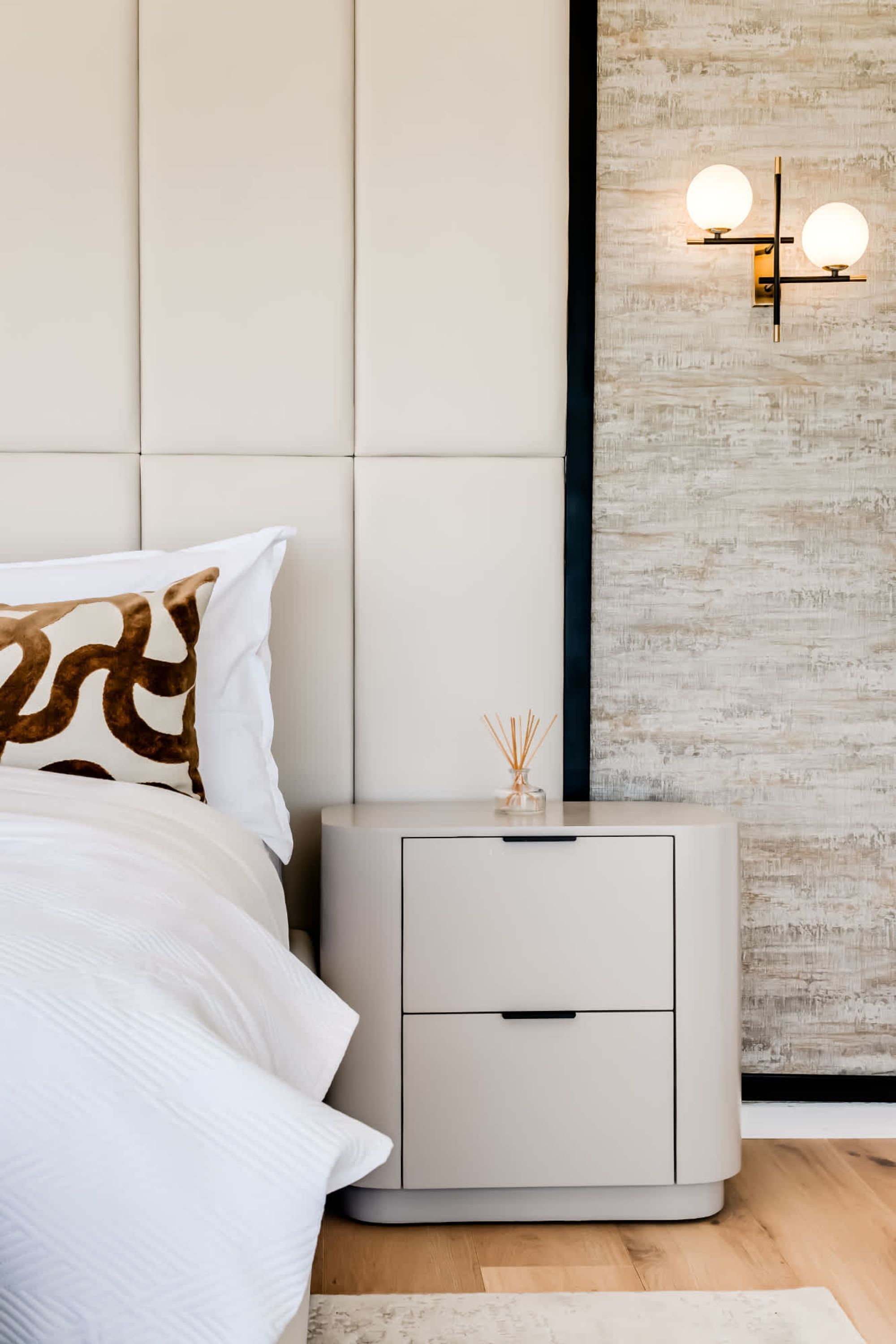 A modern bedroom with a tufted headboard, a bedside table with a drawer, and a wall-mounted light fixture.