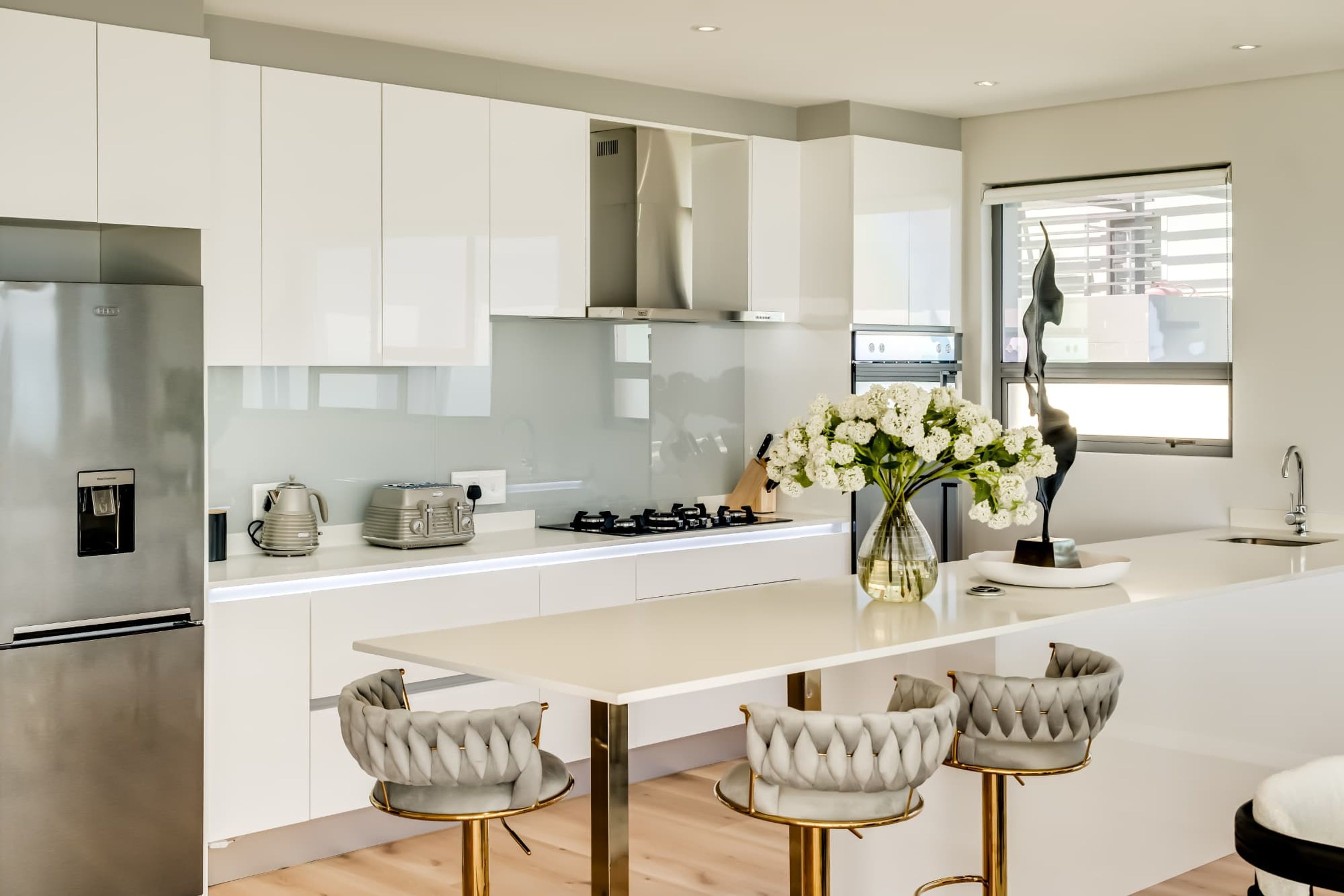 A modern kitchen with white cabinetry, stainless steel appliances, and a central island with bar stools.