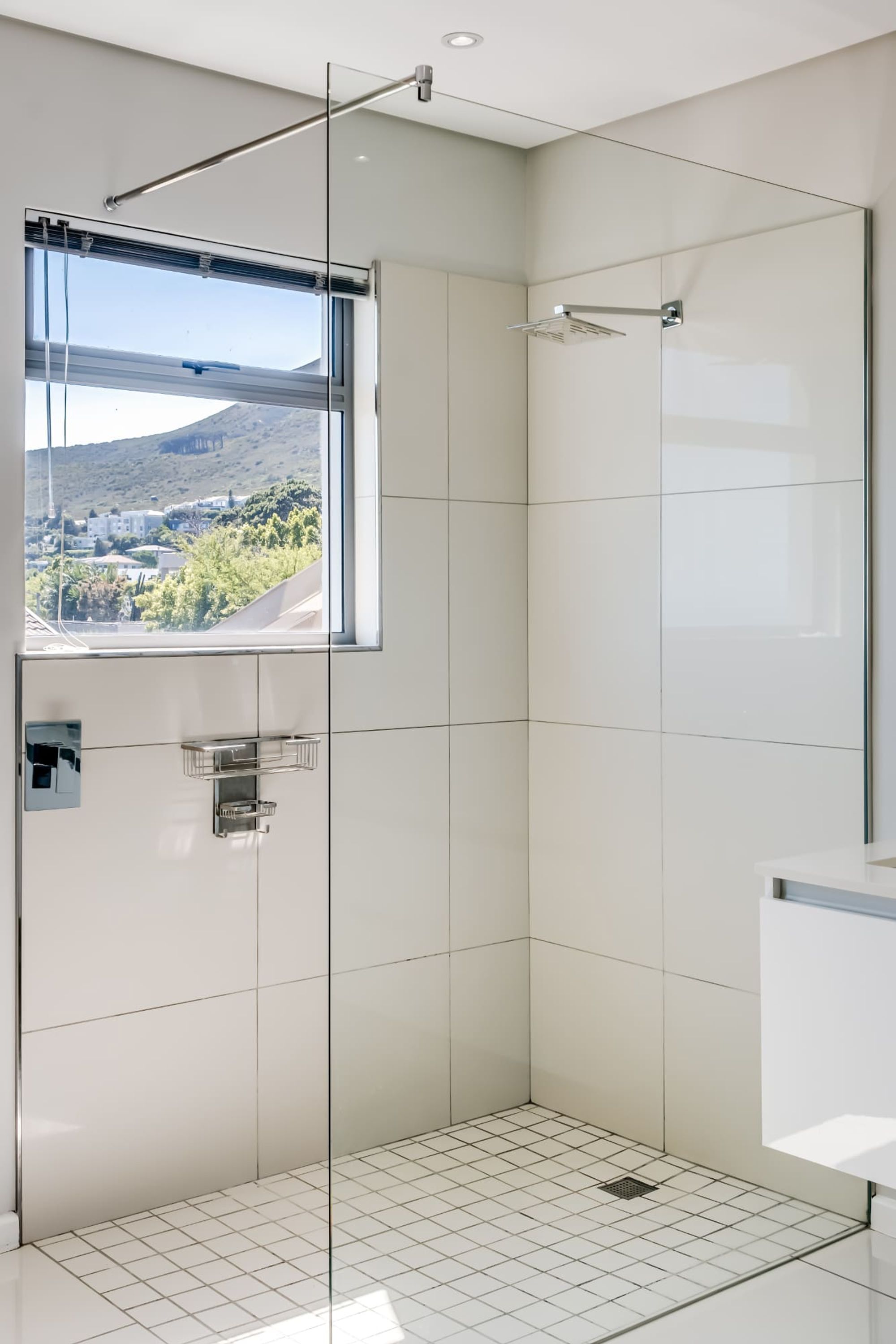 A modern shower with a glass door, a window with a view of a mountainous landscape, and a tiled floor.