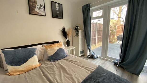 A bedroom with a bed, a nightstand, a vase with dried plants, and a window with curtains.
