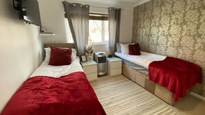 A room with two beds, a small table, a heater, and a window with curtains.