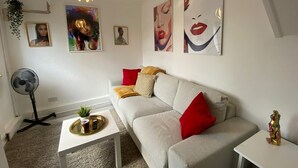 A living room with a white sofa, red and beige cushions, a small white coffee table, and a gold-framed picture on the wall.