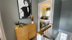 A hallway with a wooden dresser, a black and white framed artwork, and a staircase leading to a bedroom with a bed and a hanging light fixture.