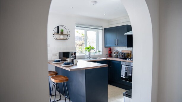 A modern kitchen with a central island, bar stools, and a window providing natural light. - Host Stay Glazier Drive (Milton Keynes)