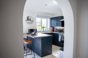 A modern kitchen with a central island, bar stools, and a window providing natural light. - Host Stay Glazier Drive (Milton Keynes)