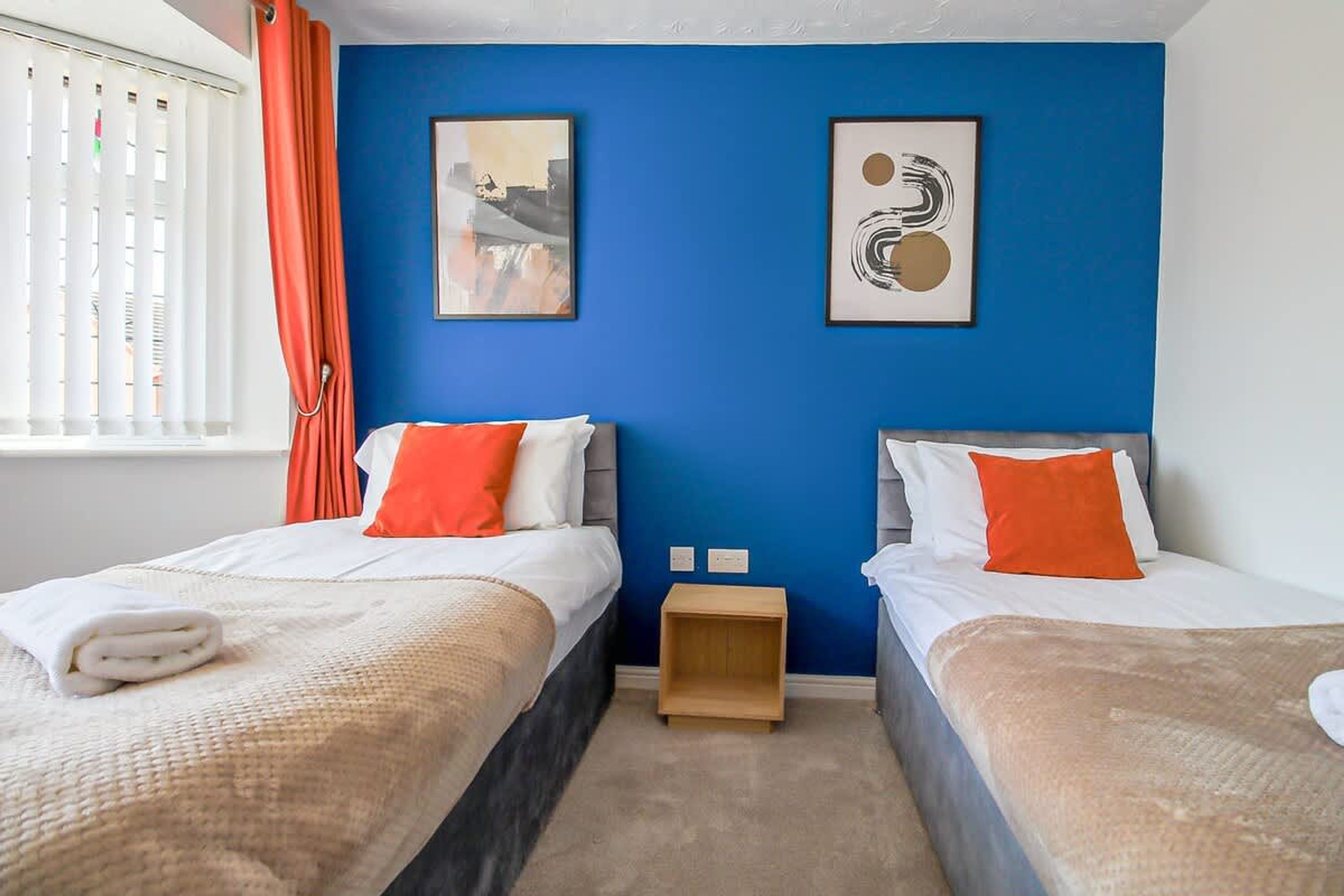 A hotel room with two beds, a blue accent wall, and artwork.