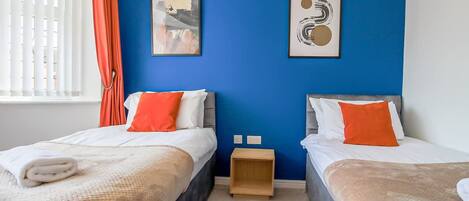 A hotel room with two beds, a blue accent wall, and artwork.