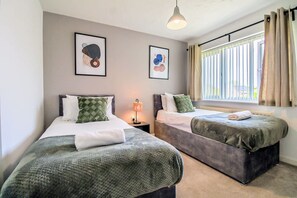 Une chambre avec deux lits, une fenêtre avec des rideaux et deux œuvres d’art encadrées accrochées au mur.