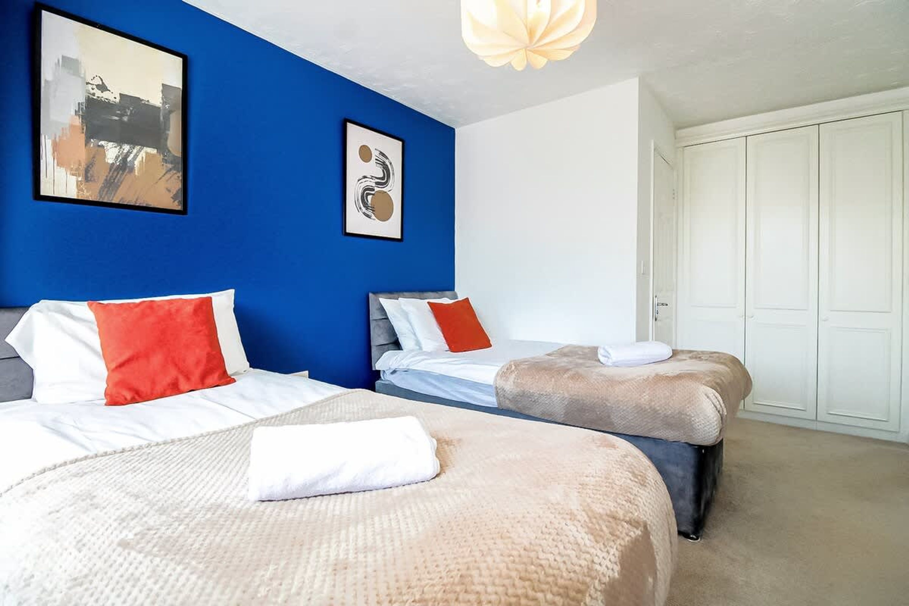 A hotel room with two beds, a blue accent wall, and a white wardrobe.