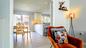 A modern interior with a dining area, kitchen, and a vibrant orange chair with a geometric pillow. - Host Stay Wiltshire Way (Milton Keynes)