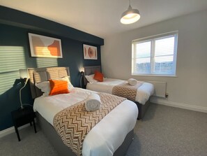 A hotel room with two beds, a window with blinds, a radiator, and artwork on the wall. - Host Stay Bluebell Close (Corby)