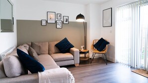 A modern living room with a sofa, a chair, a floor lamp, and framed pictures on the wall. - Host Stay Hewitt Close (Peterborough)