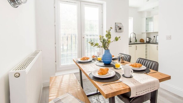 A dining area with a wooden table, chairs, and a vase with green plants. - Host Stay Davies Close (Market Harborough)
