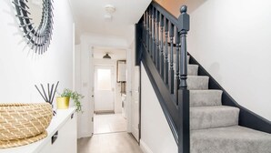 A staircase with black balusters and beige carpeted steps leading to a hallway. - Host Stay Davies Close (Market Harborough)