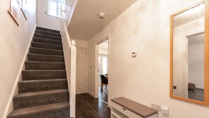Eine Treppe führt zu einer zweiten Etage, eine Bank, ein Spiegel und eine Tür sind vorhanden.