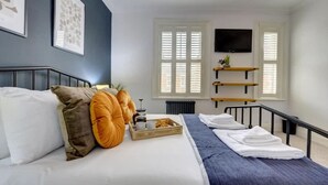Una habitación de hotel con una cama, una mesita de centro con una bandeja, un televisor montado en la pared y una ventana con persianas.