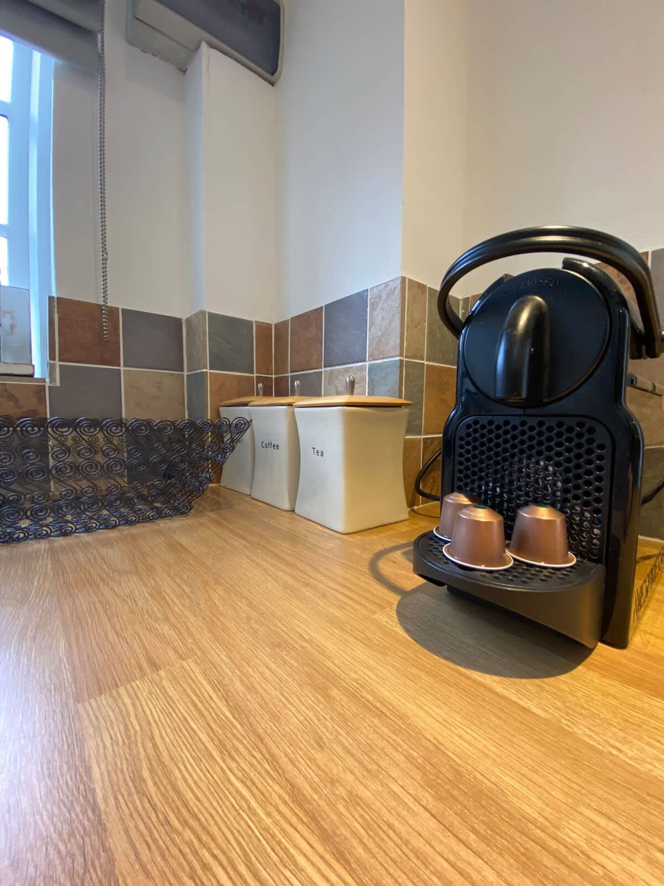 A kitchen with a coffee maker, two containers labeled 'Coffee' and 'Tea', and a decorative metal fence.