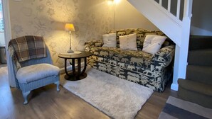 Una sala de estar con un sofá estampado, un sillón escocés, una mesita redonda y una escalera con barandillas blancas.