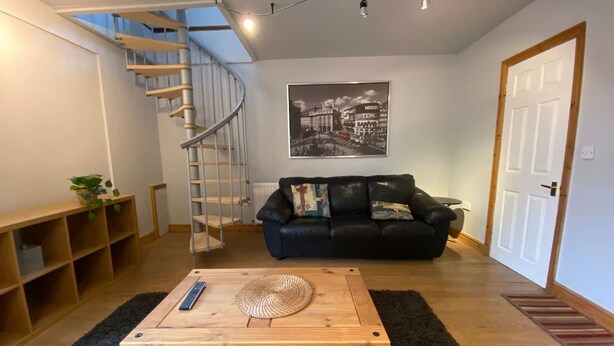A living room with a wooden coffee table, a black leather sofa, a spiral staircase, and a framed picture on the wall. - Host Stay Studley Knapp (Milton Keynes)