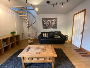 A living room with a wooden coffee table, a black leather sofa, a spiral staircase, and a framed picture on the wall. - Host Stay Studley Knapp (Milton Keynes)