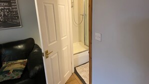 A room with a white door, a shower area, and a black leather couch. - Host Stay Studley Knapp (Milton Keynes)