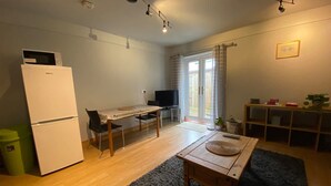 A compact kitchen with a refrigerator, a dining table with chairs, a TV, and a small shelf with items. - Host Stay Studley Knapp (Milton Keynes)