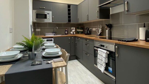 Una cucina moderna con mobili grigi, un piano di lavoro in legno, un forno a microonde integrato e un piccolo tavolo da pranzo per quattro persone.